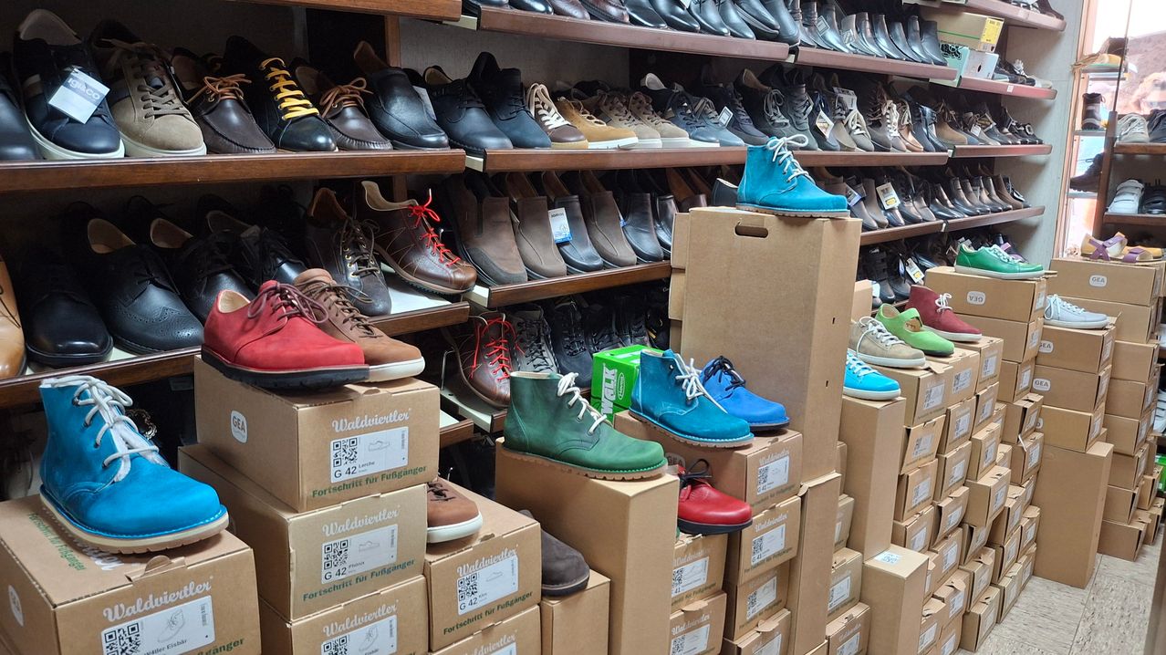 Ein Schuhgeschäft zeigt verschiedene Paar Schuhe auf Regalen und Kisten, mit mehreren Farben und Stilen, einige mit Etiketten.