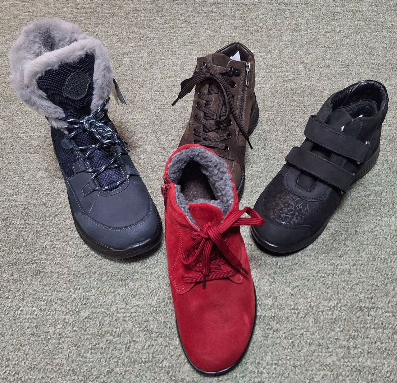 Vier Stiefel liegen auf dem Teppich: ein marineblauer Stiefel, ein roter Stiefel, ein brauner Stiefel und ein schwarzer Stiefel.