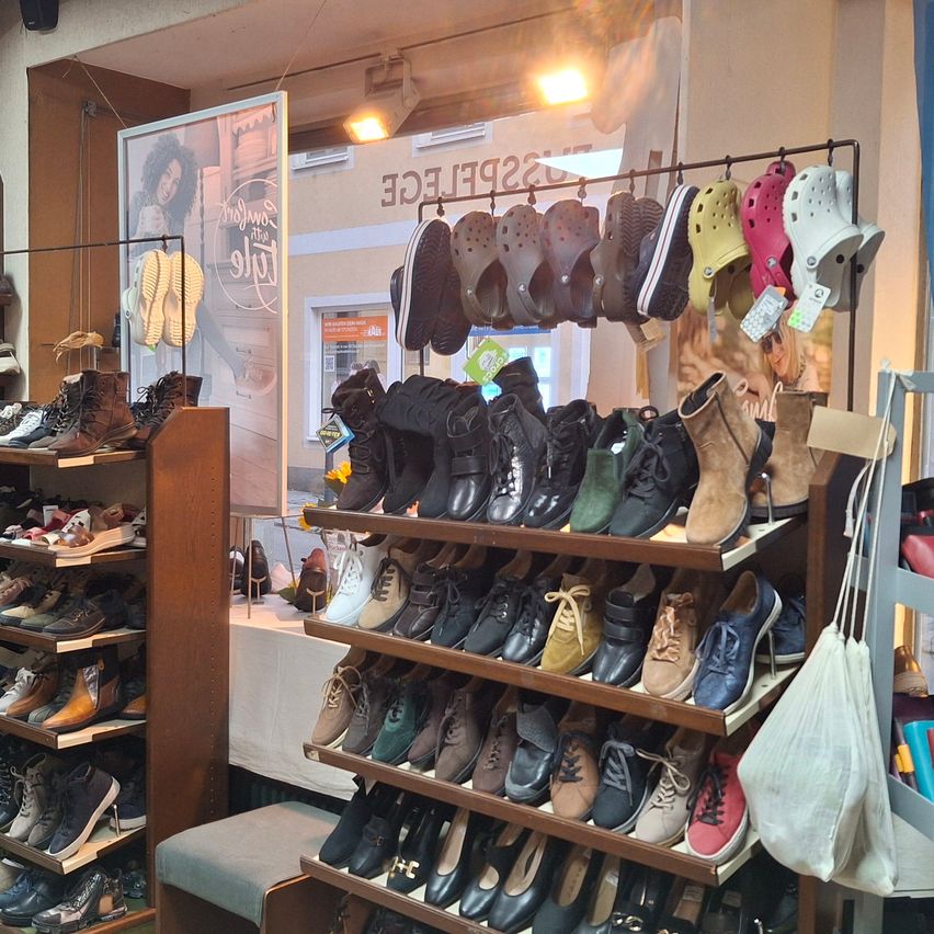 Ein Schuhgeschäft mit vielen Schuhsorten im Angebot. Ein großer Ständer hält Stiefel, Turnschuhe und Sandalen. Ein anderer Ständer hält Crocs.