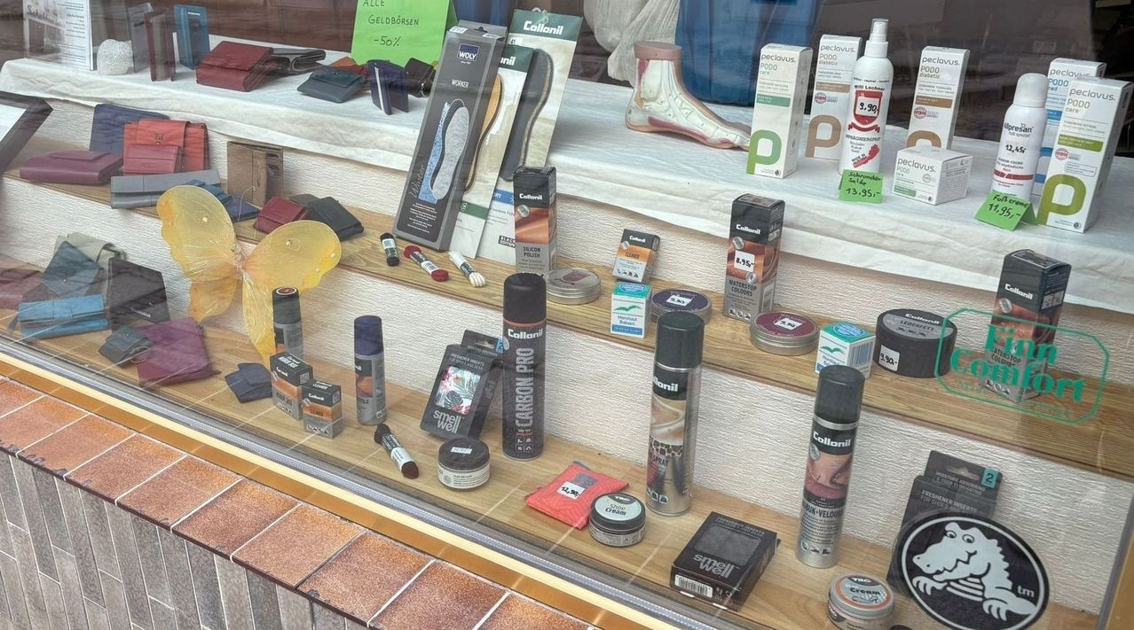 Eine Ausstellung verschiedener Schuhpflegeprodukte, einschließlich Politur, Bürsten und geruchsbeseitigenden Artikeln, auf einem Holzregal mit weißem Tuchhintergrund und einem Preisschild mit 13,95.