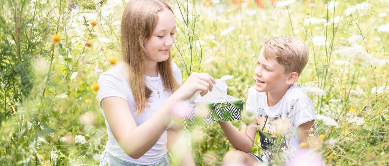Pollenschutz - Kinder die einer blühenden Wiese sitzen.