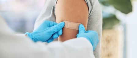 Ein medizinischer Fachmann in blauen Handschuhen legt einem Patienten einen Verband auf die Schulter.