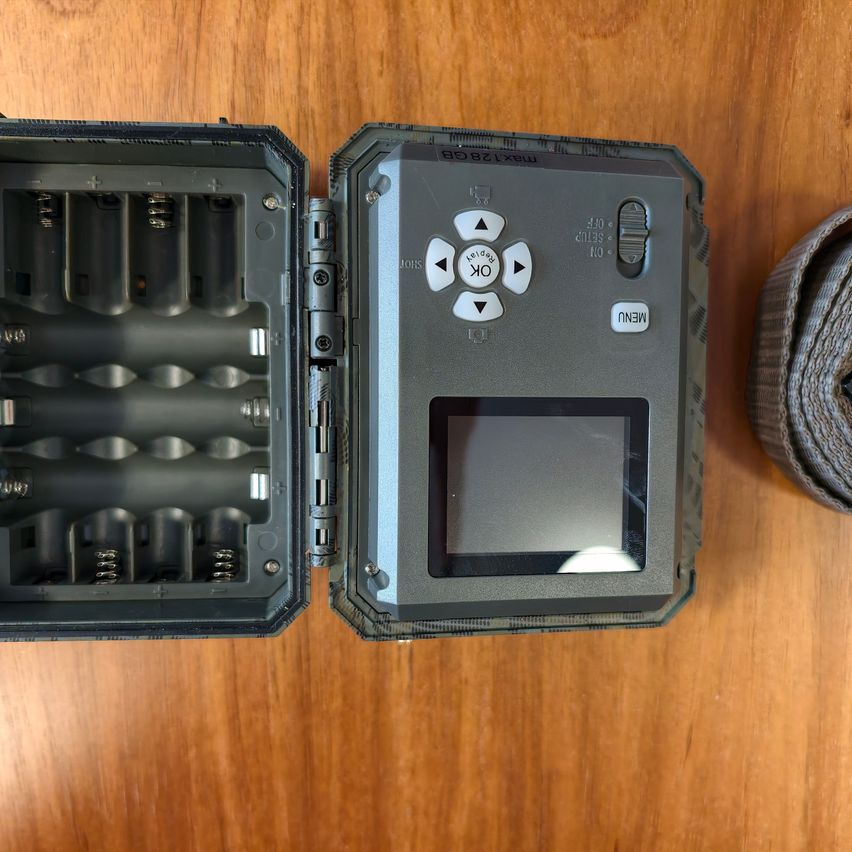 Ein offenes elektronisches Gerät mit Batteriefach und kleinem Bildschirm liegt auf einer Holzoberfläche.