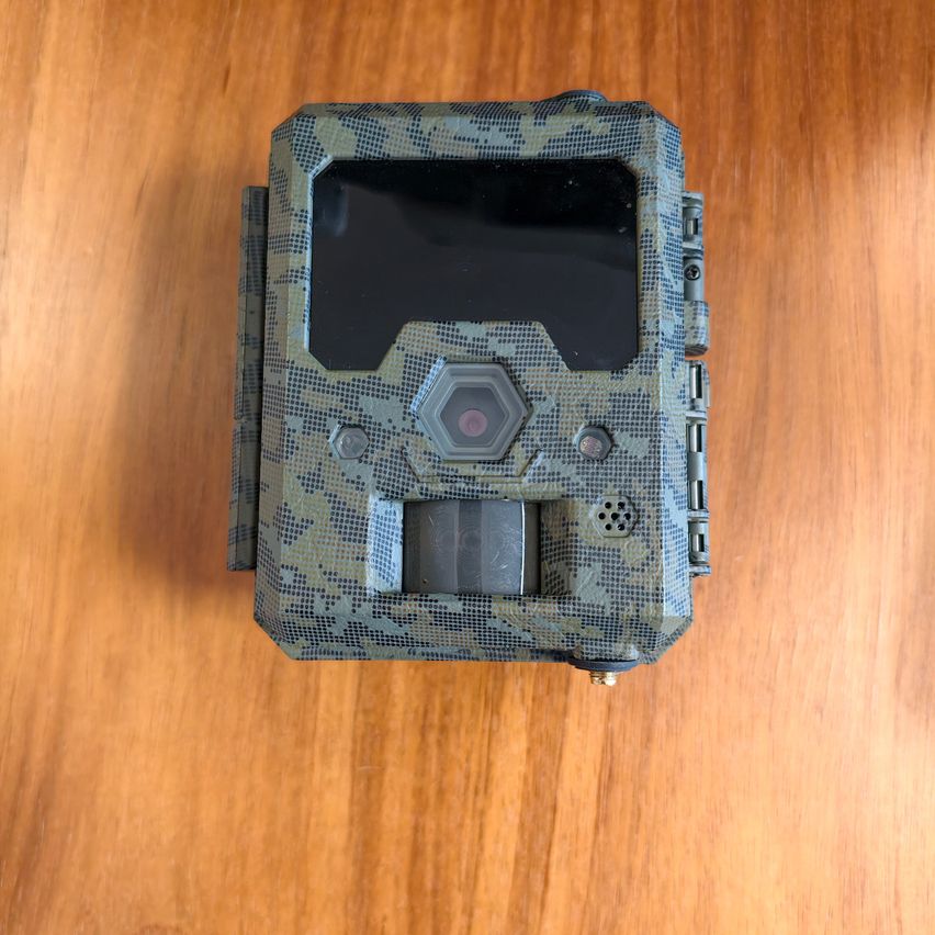 Eine Tarnmuster-Trail-Kamera mit Objektiv und Tasten liegt auf einer Holzoberfläche.