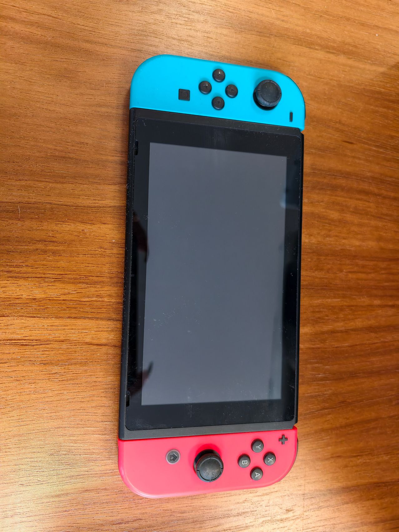 Eine Nintendo Switch Lite wird in Neonblau und Korallenrot gezeigt. Sie liegt auf einer Holzoberfläche.