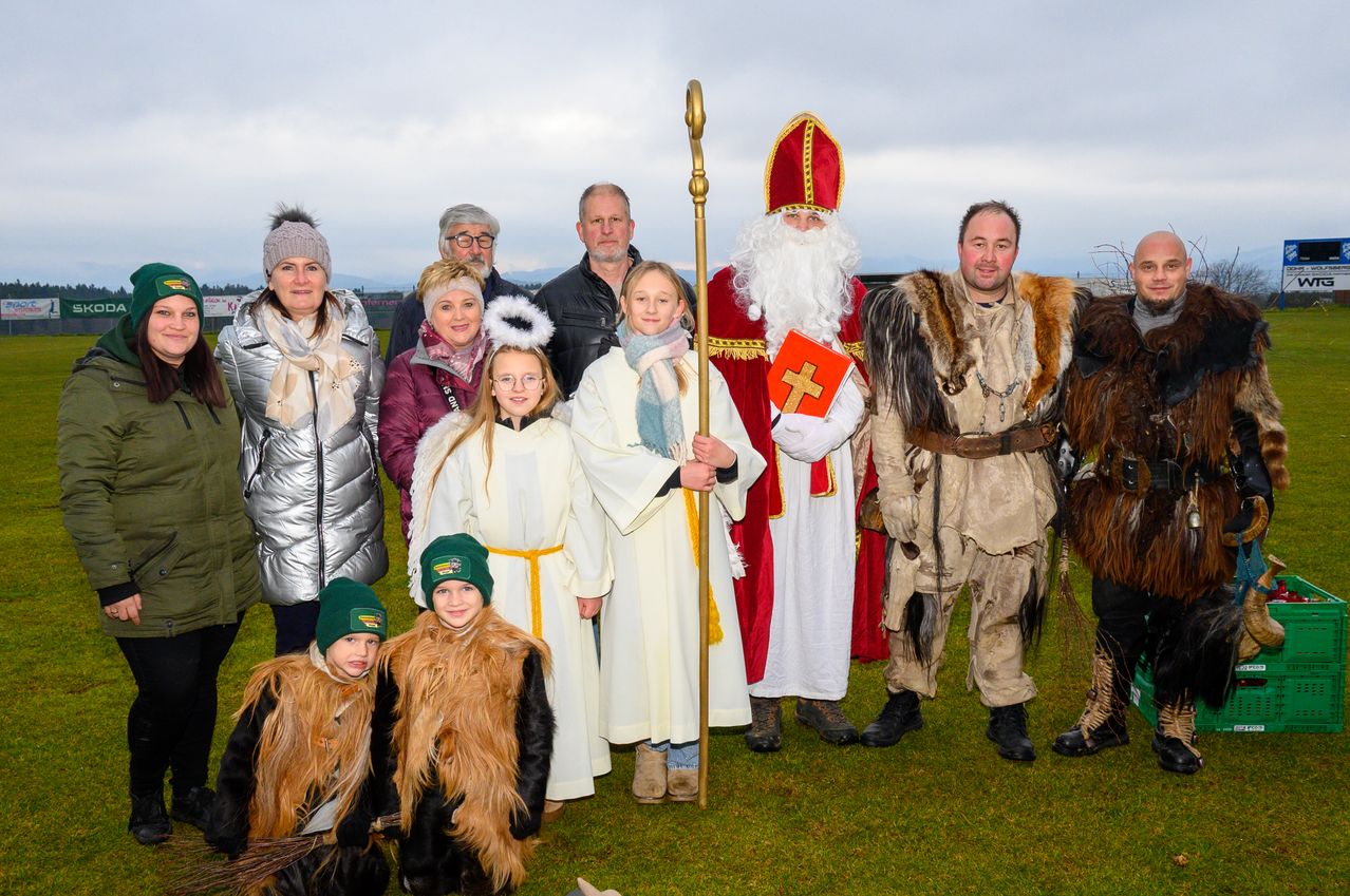Eine Gruppe von Menschen in verschiedenen Kostümen, darunter einer in einem Weihnachtsmann-Kostüm, posiert für ein Foto auf einer Rasenfläche.