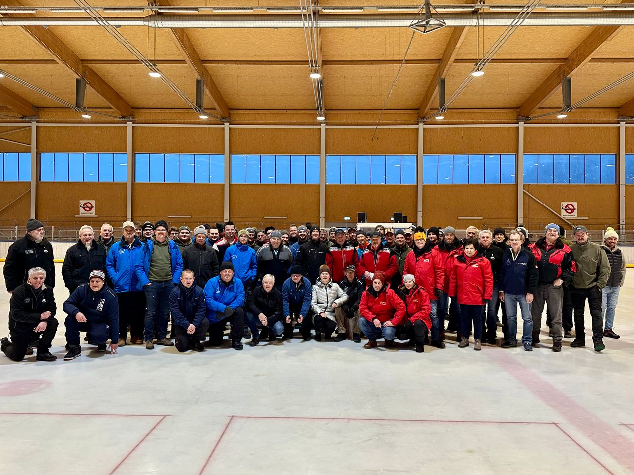 Eine Gruppe von Menschen in Winterkleidung posiert für ein Foto in einem Innenraum mit weißem Boden und großen Fenstern.