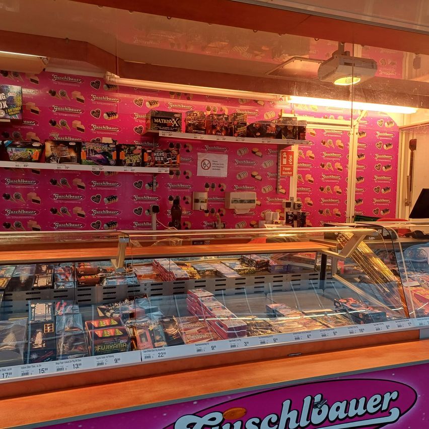 Innenbereich eines Süßwarenladens mit einer Glasvitrine voller Süßigkeiten, rosa Wänden, die mit verschiedenen Süßigkeiten und Herzdesigns verziert sind, und einer Projektorlampe an der Decke.