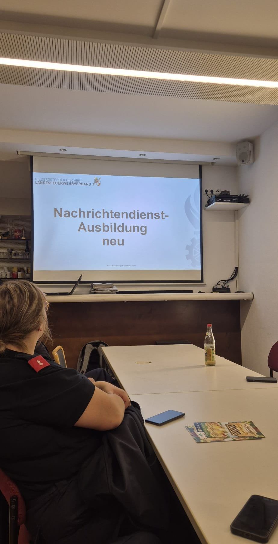 Eine Frau besucht eine Präsentation über neue Nachrichtendienstausbildung, die auf einer Leinwand mit einer weißen Wand dahinter projiziert wird.