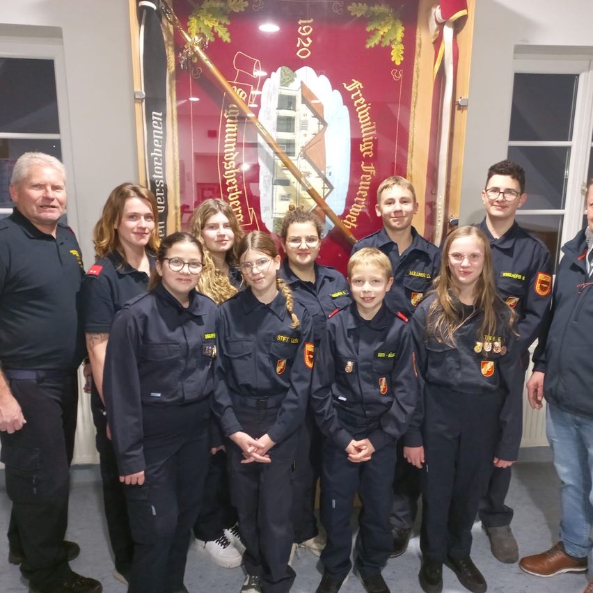 Eine Gruppe junger Menschen in Uniformen, wahrscheinlich Teil einer Jugendorganisation, posiert für ein Foto vor einem Banner mit deutschem Text. Sie werden von einigen Erwachsenen begleitet.