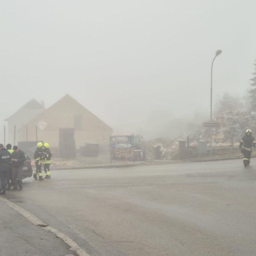 Eine Gruppe von Menschen steht in einem nebligen Bereich, möglicherweise in der Nähe eines Gebäudes. Ein Polizeibeamter ist anwesend. Einige Personen tragen Helme und Uniformen.