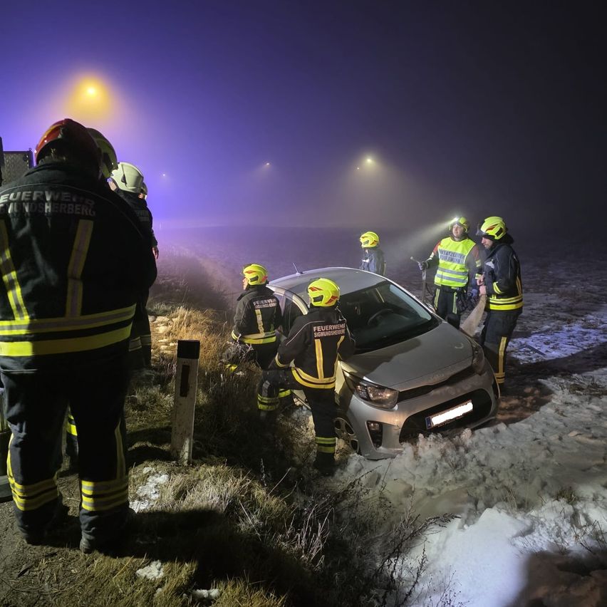 Eine Gruppe von Feuerwehrleuten in Uniform kümmert sich bei Nacht um einen Autounfall auf einer verschneiten Straße.