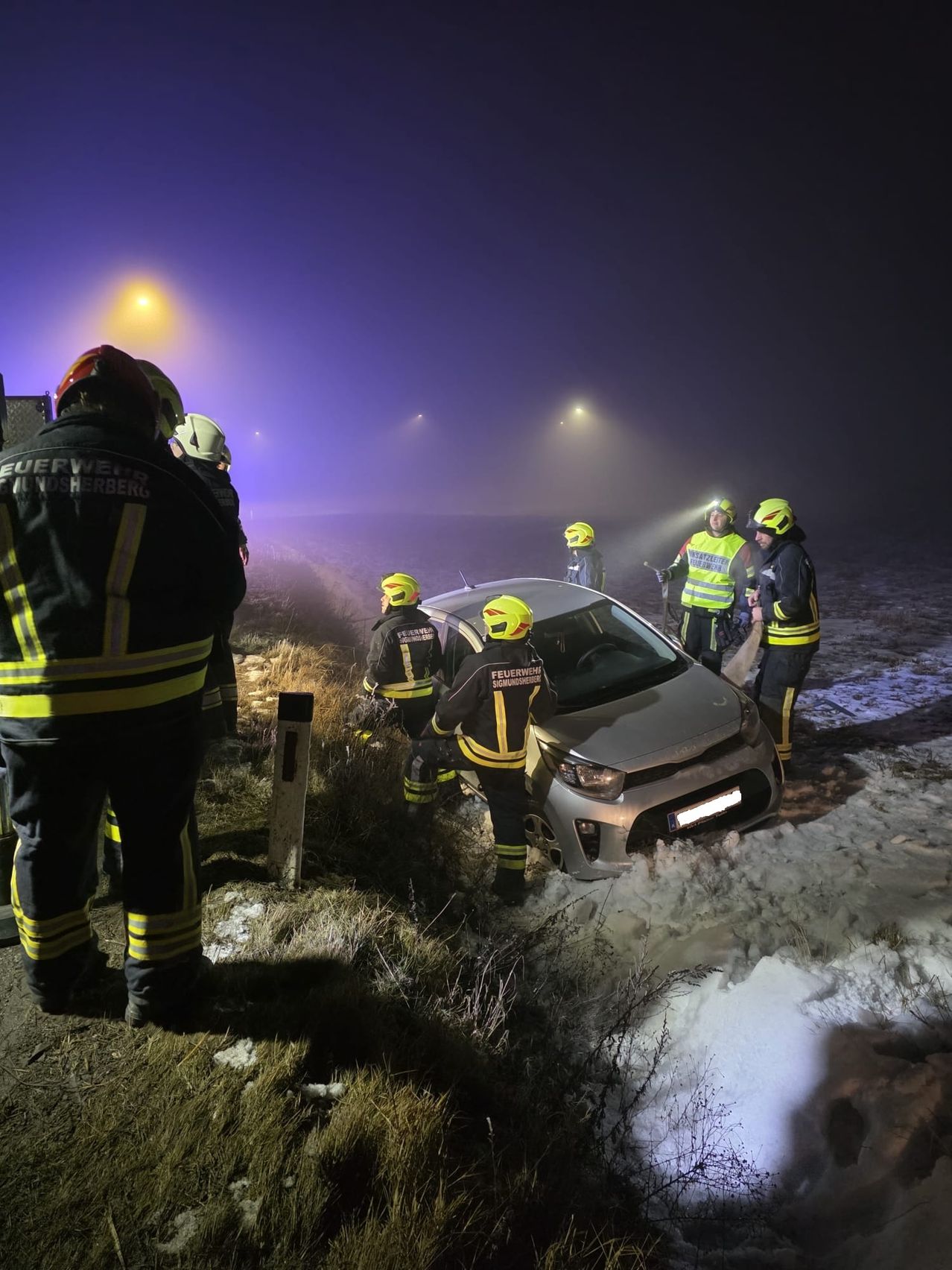 Eine Gruppe von Feuerwehrleuten in Uniform kümmert sich bei Nacht um einen Autounfall auf einer verschneiten Straße.
