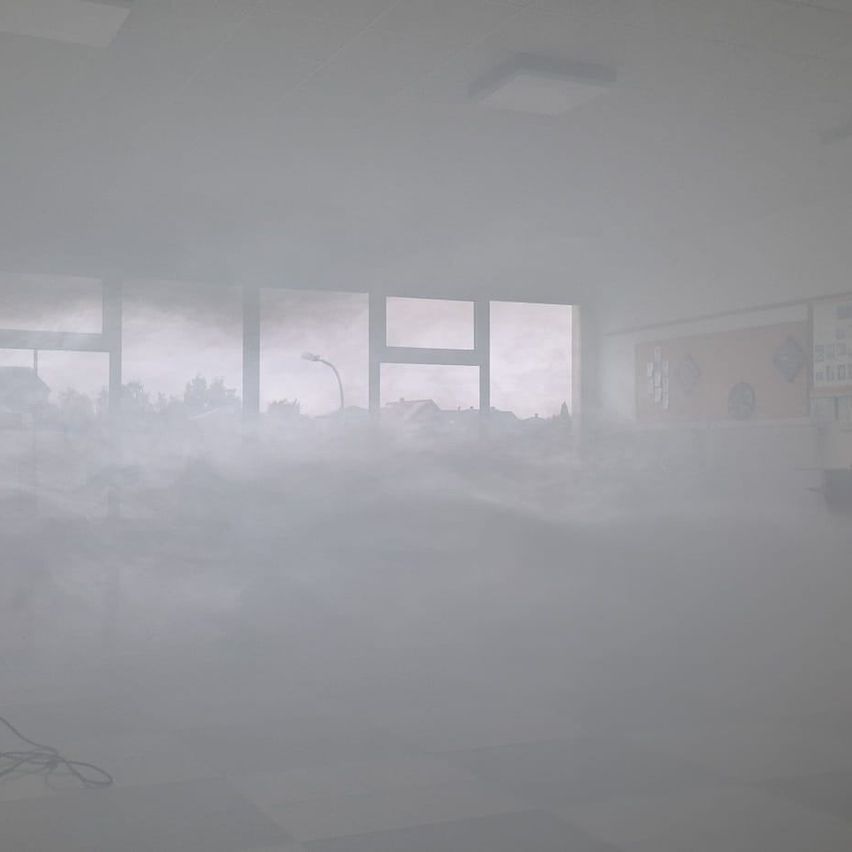 Ein verrauchter Innenraum mit drei Fenstern, die einen Blick auf eine Straße mit Straßenlaterne und Bäumen draußen bieten.