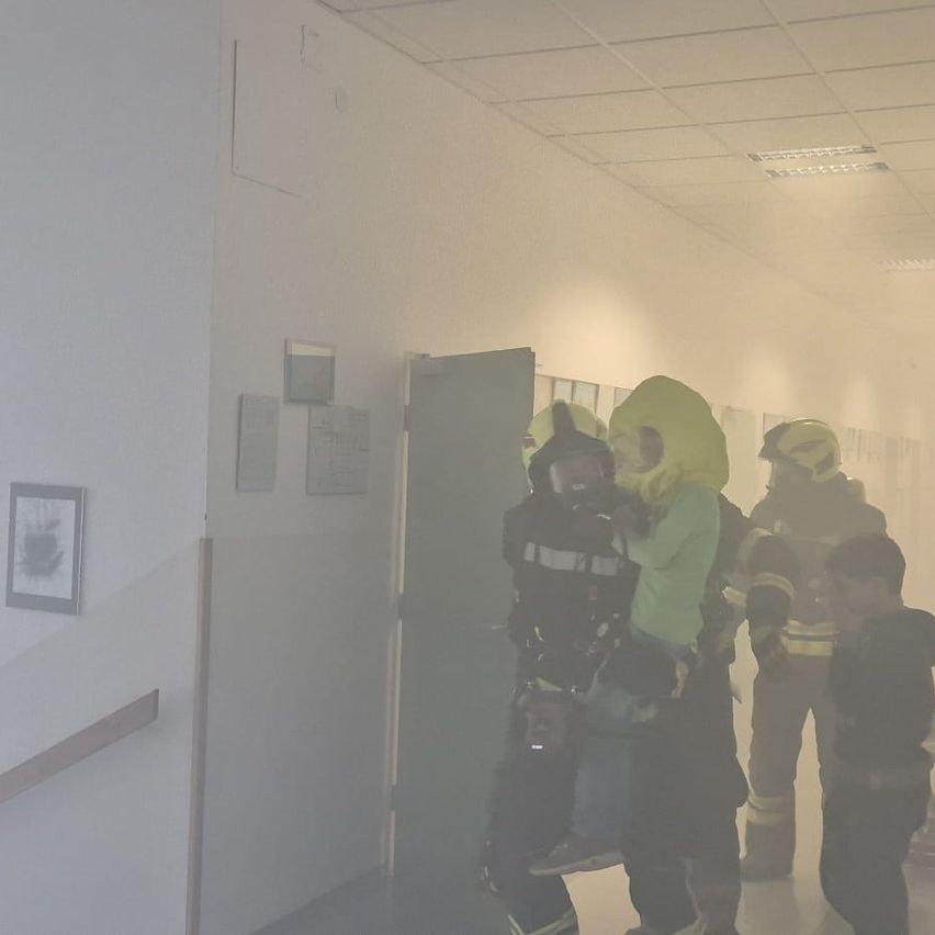 Feuerwehrleute evakuieren ein Kind in einem Flur mit dickem Rauch, das Kind trägt eine grüne Jacke.