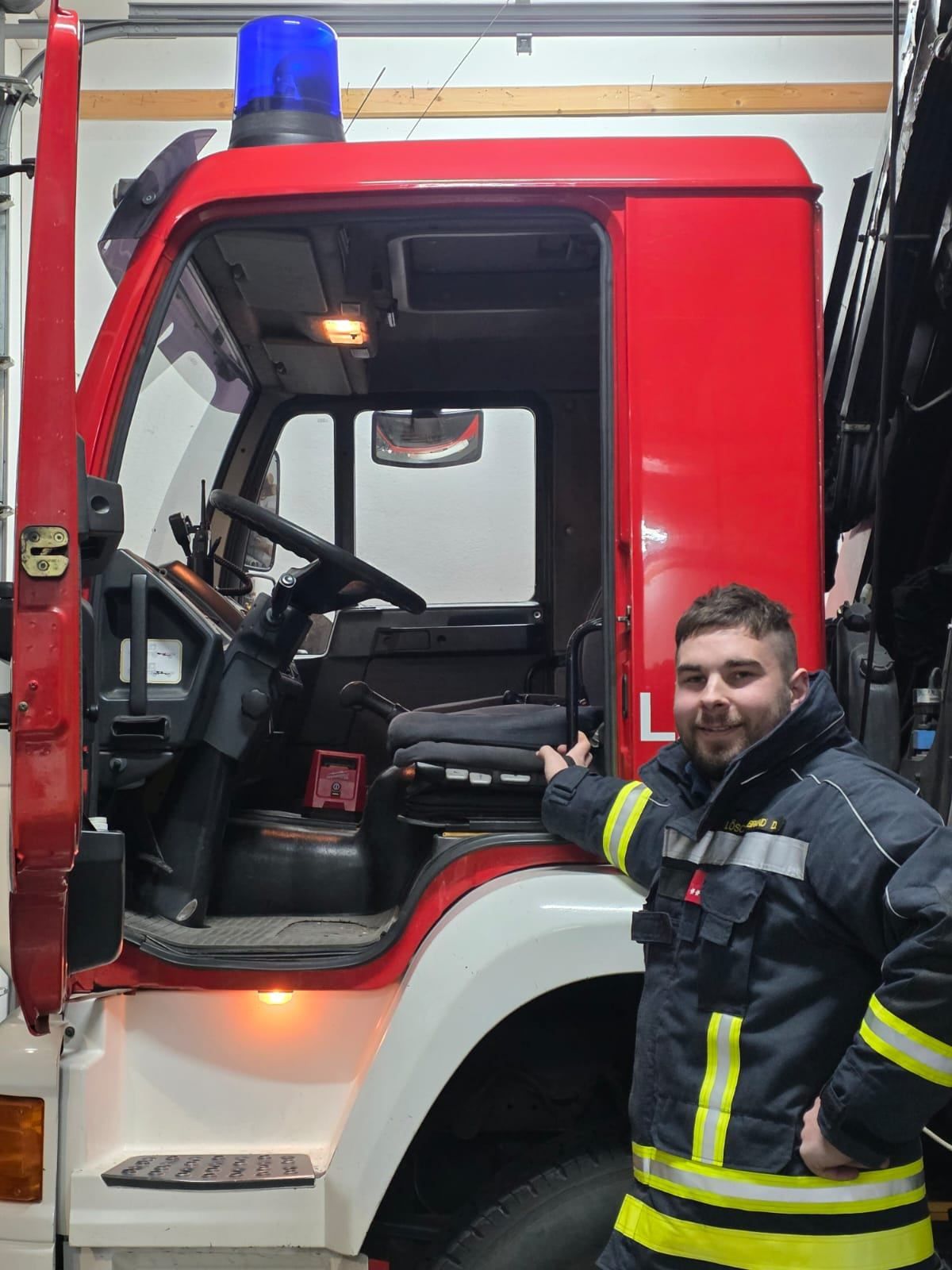 Ein Mann in einer Feuerwehruniform steht neben einem roten Feuerwehrauto mit offener Tür und zeigt das Innere.