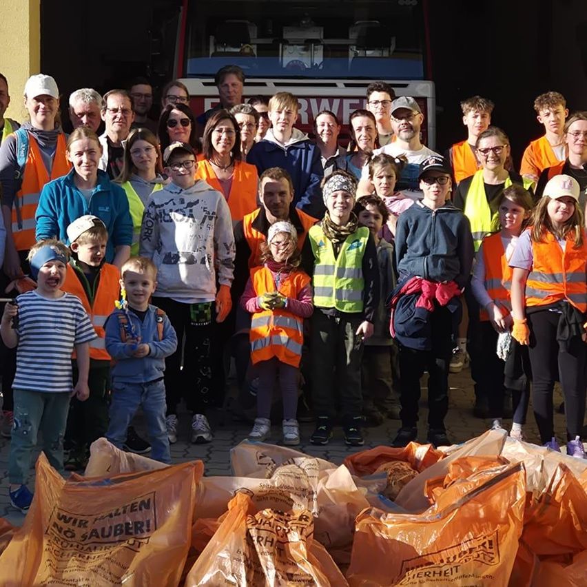 Eine Gruppe von Menschen in Warnwesten, einige mit Mützen, stehen vor einem Fahrzeug. Vor ihnen befinden sich Müllsäcke.