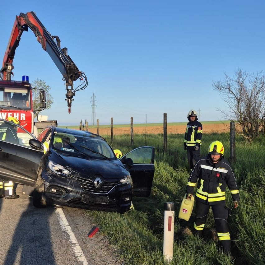 Feuerwehrleute retten eine Person aus einem beschädigten Auto. Das Auto steht am Straßenrand, mit offener Tür.