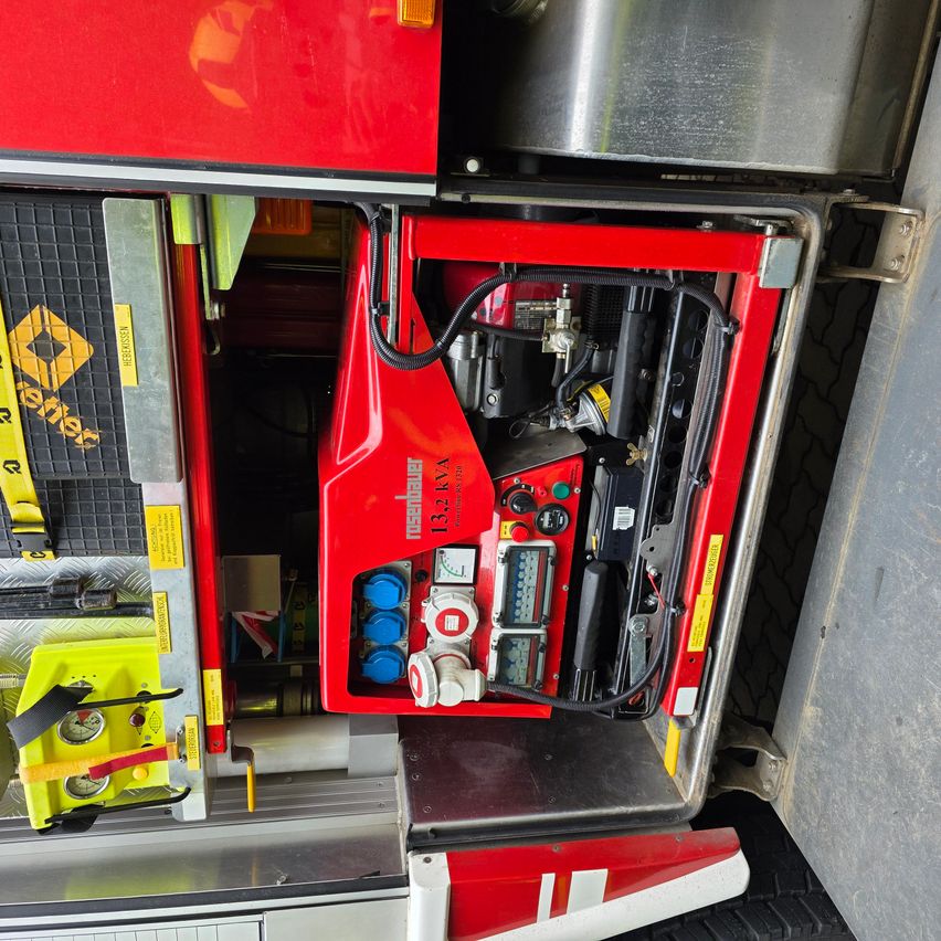 Ein roter Notfallgenerator mit verschiedenen Schaltern und Zählern ist an der Seite eines Fahrzeugs, möglicherweise eines Feuerwehrwagens, geöffnet.