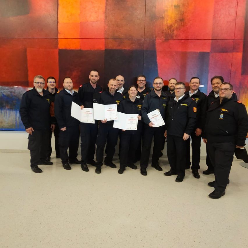 Eine Gruppe von Personen in Uniform posiert für ein Foto, während sie Urkunden vor einer farbenfrohen Wand halten.