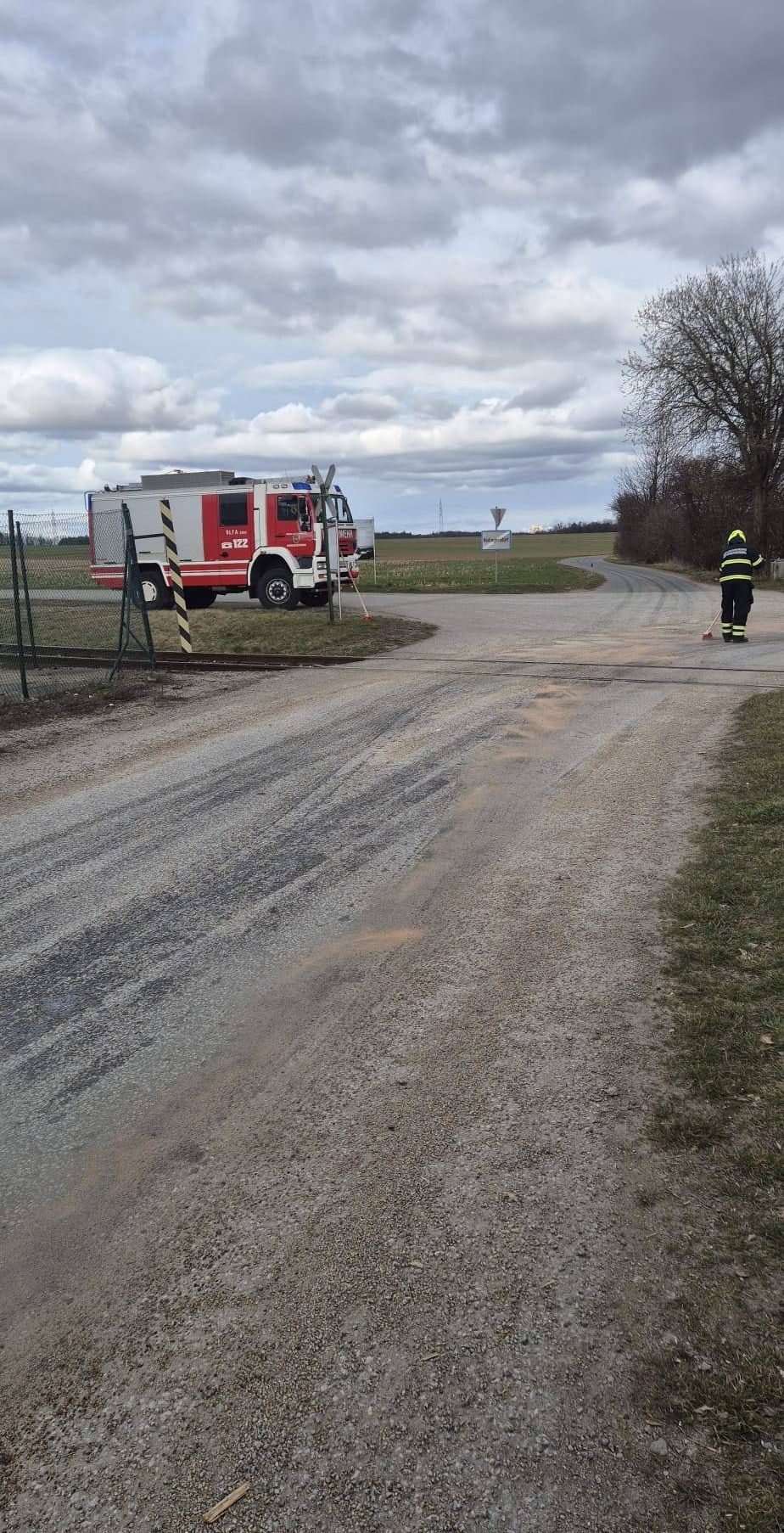 Ein Feuerwehrmann steht an einer Straßenkreuzung, hält einen Besen und ein Feuerwehrauto steht in der Nähe.