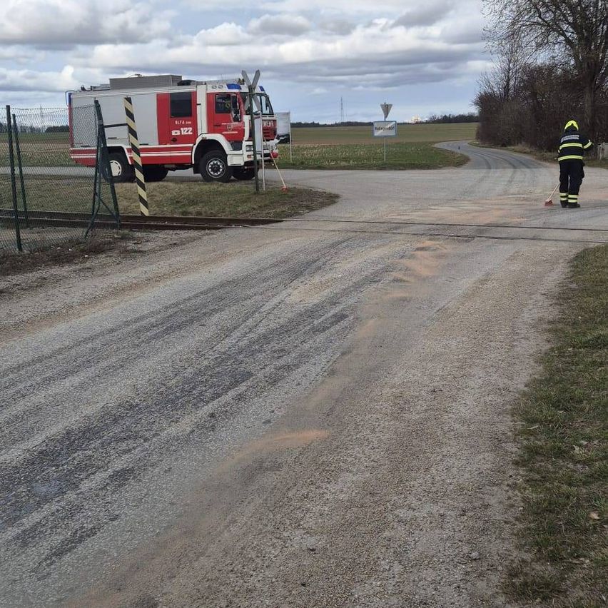 Ein Feuerwehrmann steht an einer Straßenkreuzung, hält einen Besen und ein Feuerwehrauto steht in der Nähe.