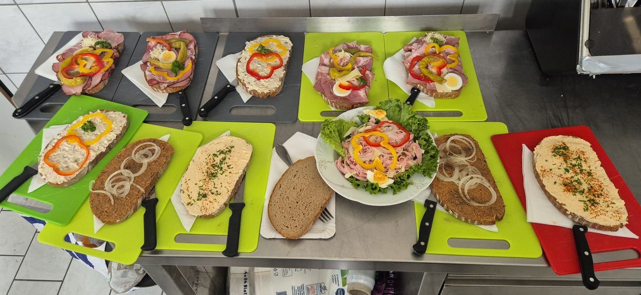 Ein Tisch zeigt verschiedene Sandwiches und einen Salat auf grünen Schneidbrettern. Jedes Sandwich hat verschiedene Beläge, einschließlich Schinken, Käse und Gemüse. Ein Teller mit Salat und eine Gabel sind ebenfalls vorhanden.