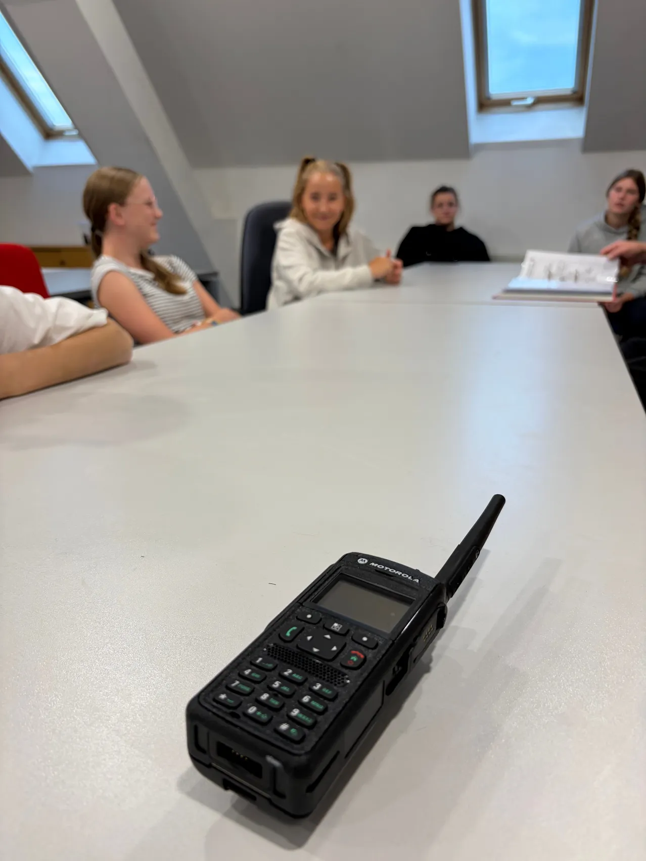 Ein Motorola-Funkgerät liegt auf einem Tisch, um den vier Personen sitzen. Das Funkgerät ist schwarz mit einer Tastatur und Antenne.