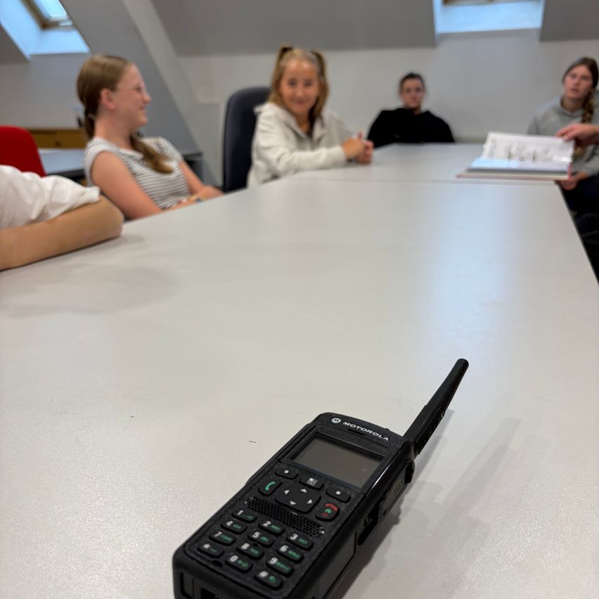 Ein Motorola-Funkgerät liegt auf einem Tisch, um den vier Personen sitzen. Das Funkgerät ist schwarz mit einer Tastatur und Antenne.