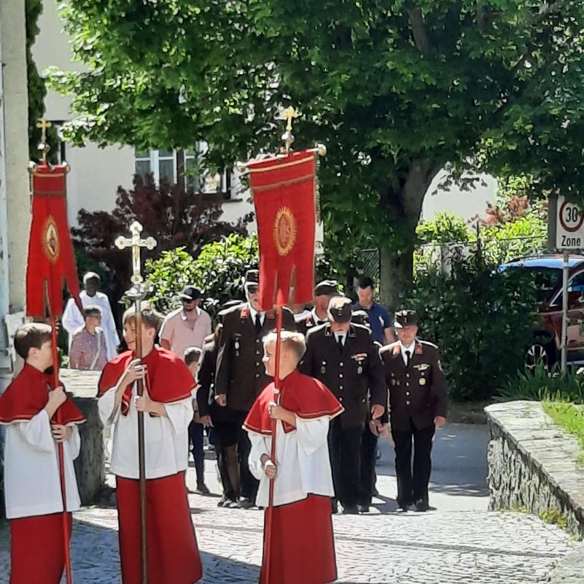 Eine Prozession mit jungen Messdienern in roten und weißen Gewändern, die Fahnen und ein Kreuz tragen, gefolgt von Militäroffizieren in Uniform.