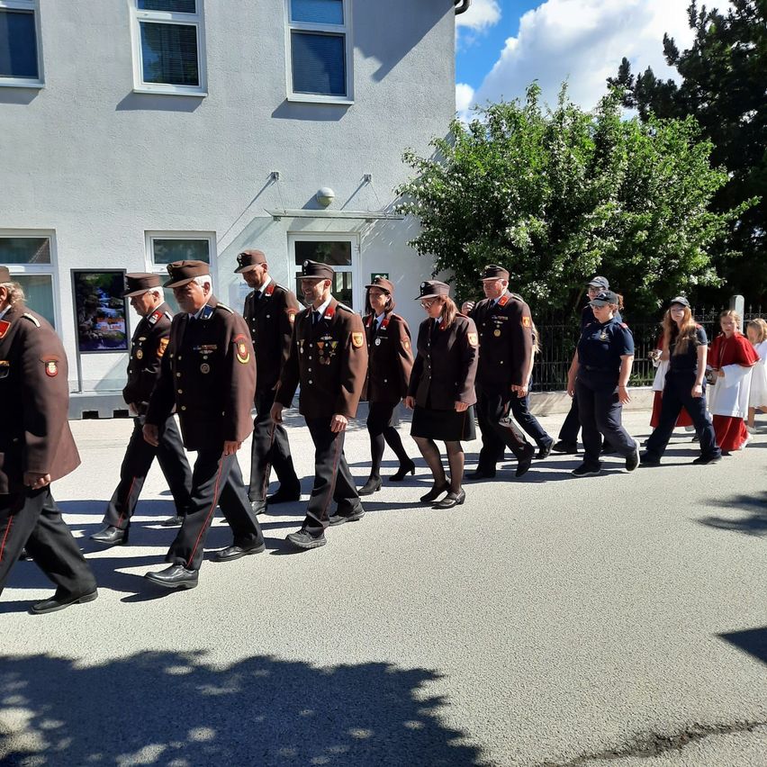 Eine Gruppe uniformierter Personen, möglicherweise Militär, die bei einer Parade auf einer Straße gehen. Sie stehen in Reihen, tragen Hüte und Schuhe.