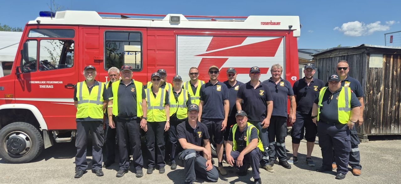 Eine Gruppe Feuerwehrleute in Uniform und Warnwesten posiert vor einem roten Rosenbauer-Feuerwehrfahrzeug.