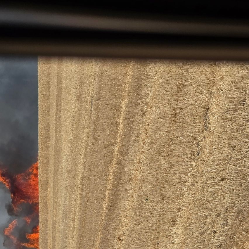 Ein Feld mit Heuballen brennt, mit Flammen und Rauch, die im linken Teil des Bildes aufsteigen.