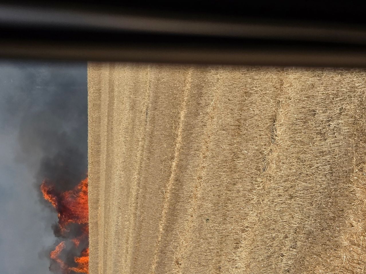 Ein Feld mit Heuballen brennt, mit Flammen und Rauch, die im linken Teil des Bildes aufsteigen.