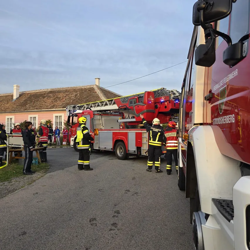 Eine Gruppe von Feuerwehrleuten steht um einen roten Feuerwehrwagen mit ausgefahrener Leiter herum. Sie tragen gelbe und schwarze Uniformen.