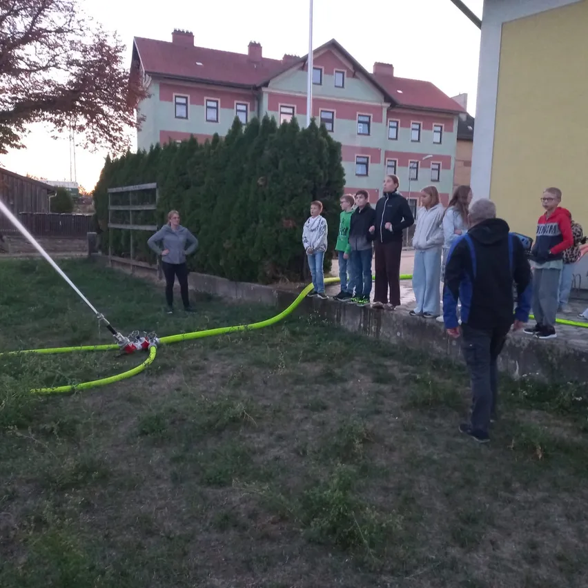 Eine Gruppe von Menschen steht um einen gelben Schlauch auf dem Rasen, mit einem Gebäude im Hintergrund.