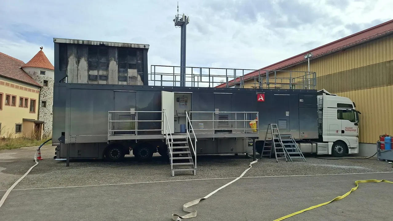 Ein großer schwarzer Anhänger mit einem weißen LKW, geparkt vor einem Gebäude mit rotem Dach.
