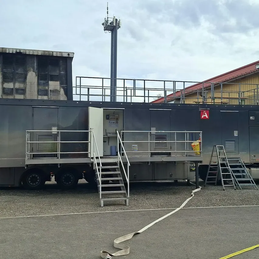 Ein großer schwarzer Anhänger mit einem weißen LKW, geparkt vor einem Gebäude mit rotem Dach.