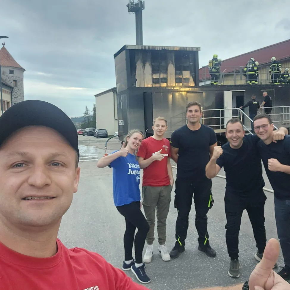 Eine Gruppe von Menschen steht vor einem Gebäude mit einem geparkten Feuerwehrwagen.