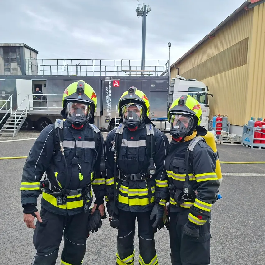 Drei Feuerwehrleute in voller Ausrüstung stehen vor einem Gebäude.