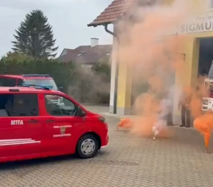 Ein roter Feuerwehrwagen ist vor einer Feuerwache geparkt, aus der Rauch austritt.