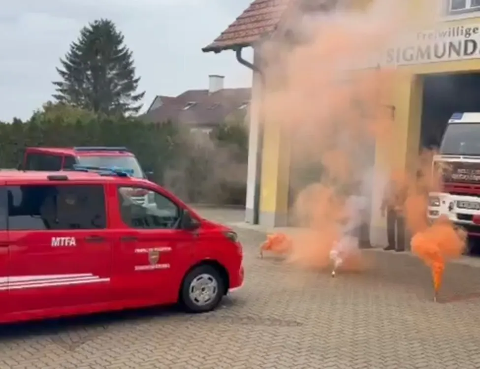 Ein roter Feuerwehrwagen ist vor einer Feuerwache geparkt, aus der Rauch austritt.