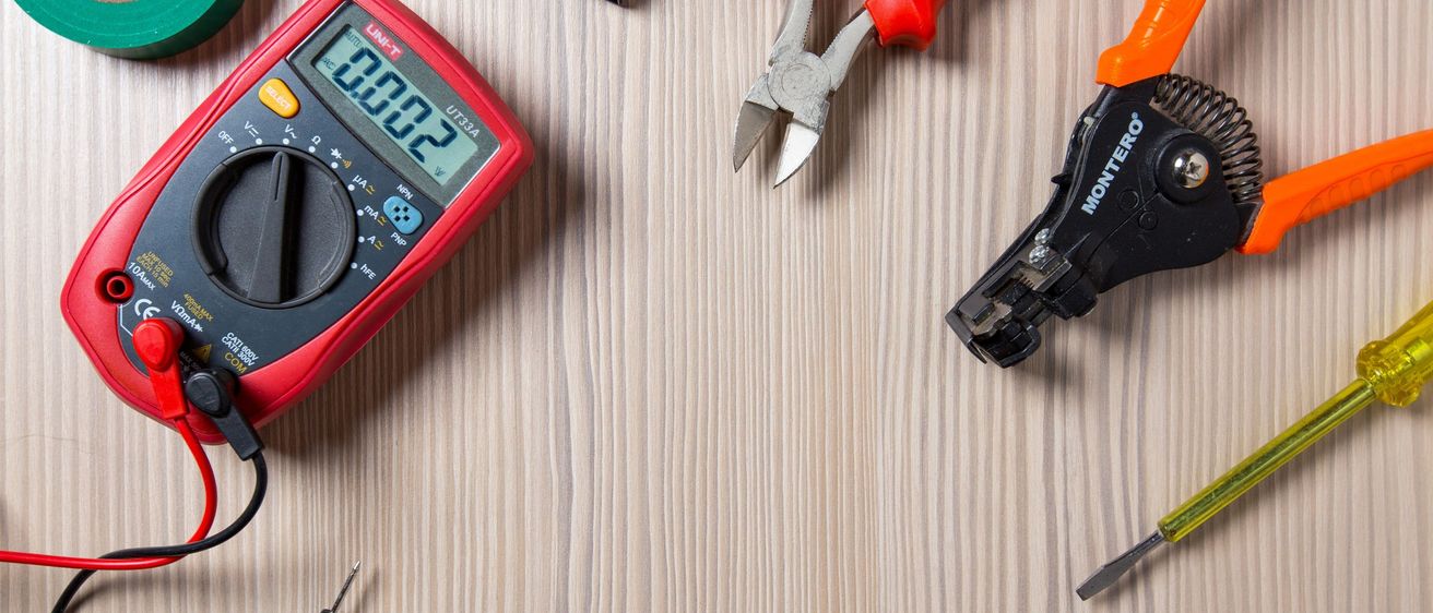 Ein Multimeter, Drahtschneider, Zangen und andere Werkzeuge liegen auf einer Holzoberfläche.