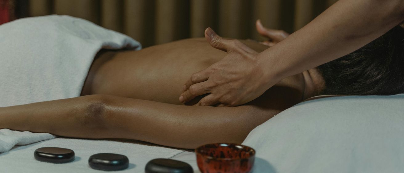Eine Person erhält eine Massage mit heißen Steinen auf einem weißen Handtuch. Die Hand des Masseurs liegt auf dem Rücken der Person.