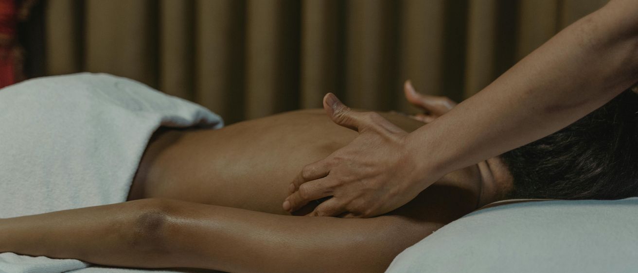 Eine Person erhält eine Massage mit heißen Steinen auf einem weißen Handtuch. Die Hand des Masseurs liegt auf dem Rücken der Person.