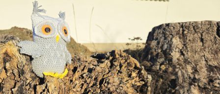 Eine gehäkelt Puppe von einem Uhu sitzt auf einem Baumstumpf, mit einem verwischten weißen Hintergrund.