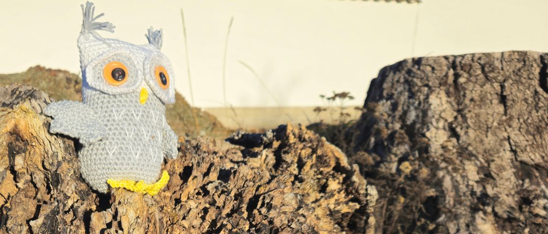 Eine gehäkelt Puppe von einem Uhu sitzt auf einem Baumstumpf, mit einem verwischten weißen Hintergrund.