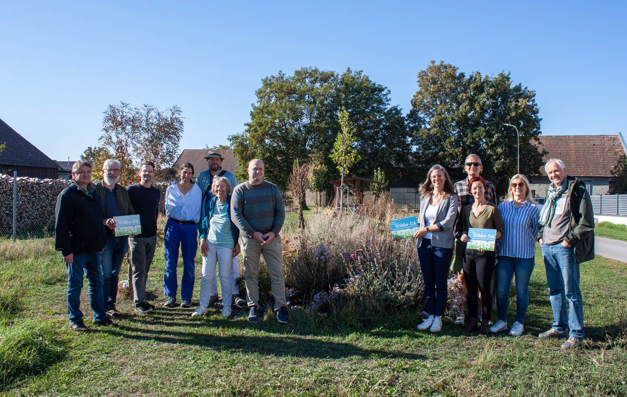 Eine Gruppe von Menschen steht auf einem Feld mit einem Baum in der Mitte. Sie halten alle ein Buch und lächeln.