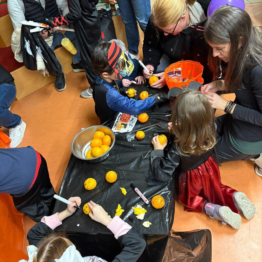 Kinder in Kostümen schnitzen Kürbisse mit Erwachsenen an einem Tisch voller orangefarbener Kürbisse, umgeben von einer Menge.