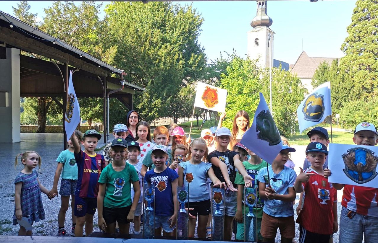 Eine Gruppe von Kindern und Erwachsenen steht in einer Reihe, hält Flaggen und lächelt für ein Foto in einem Park mit einer Kirche im Hintergrund.